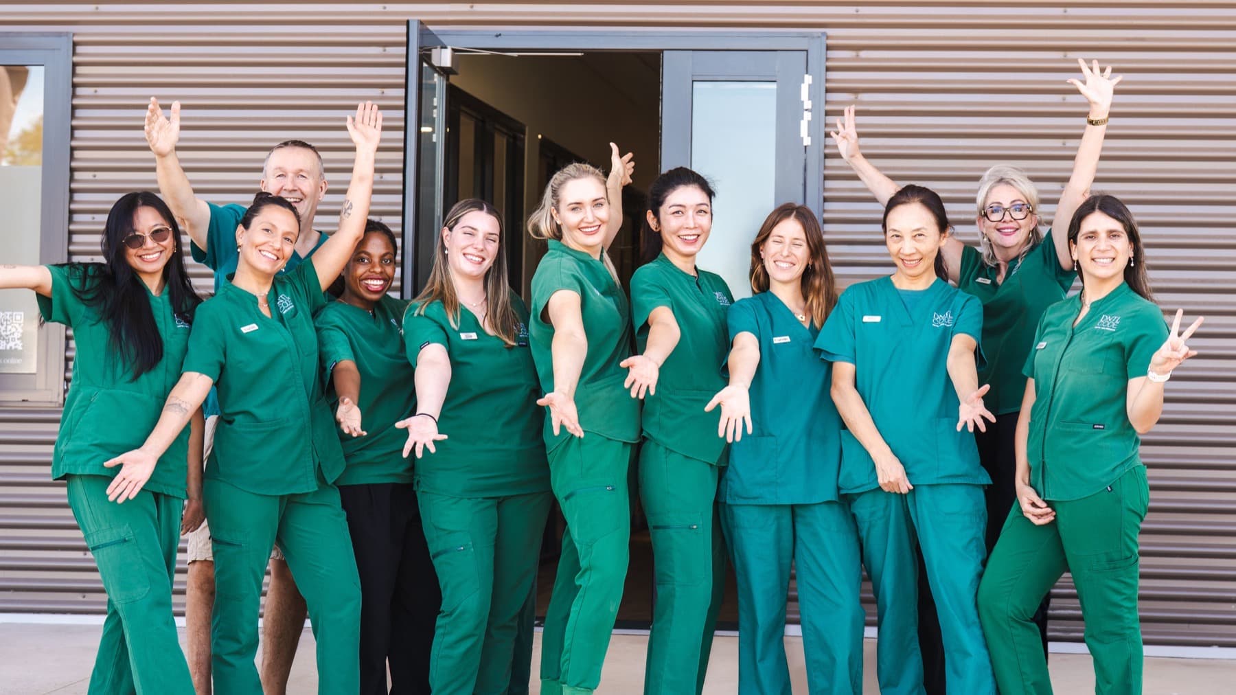 The DNTL Code team in green scrubs, arms out, laughing outside the clinic