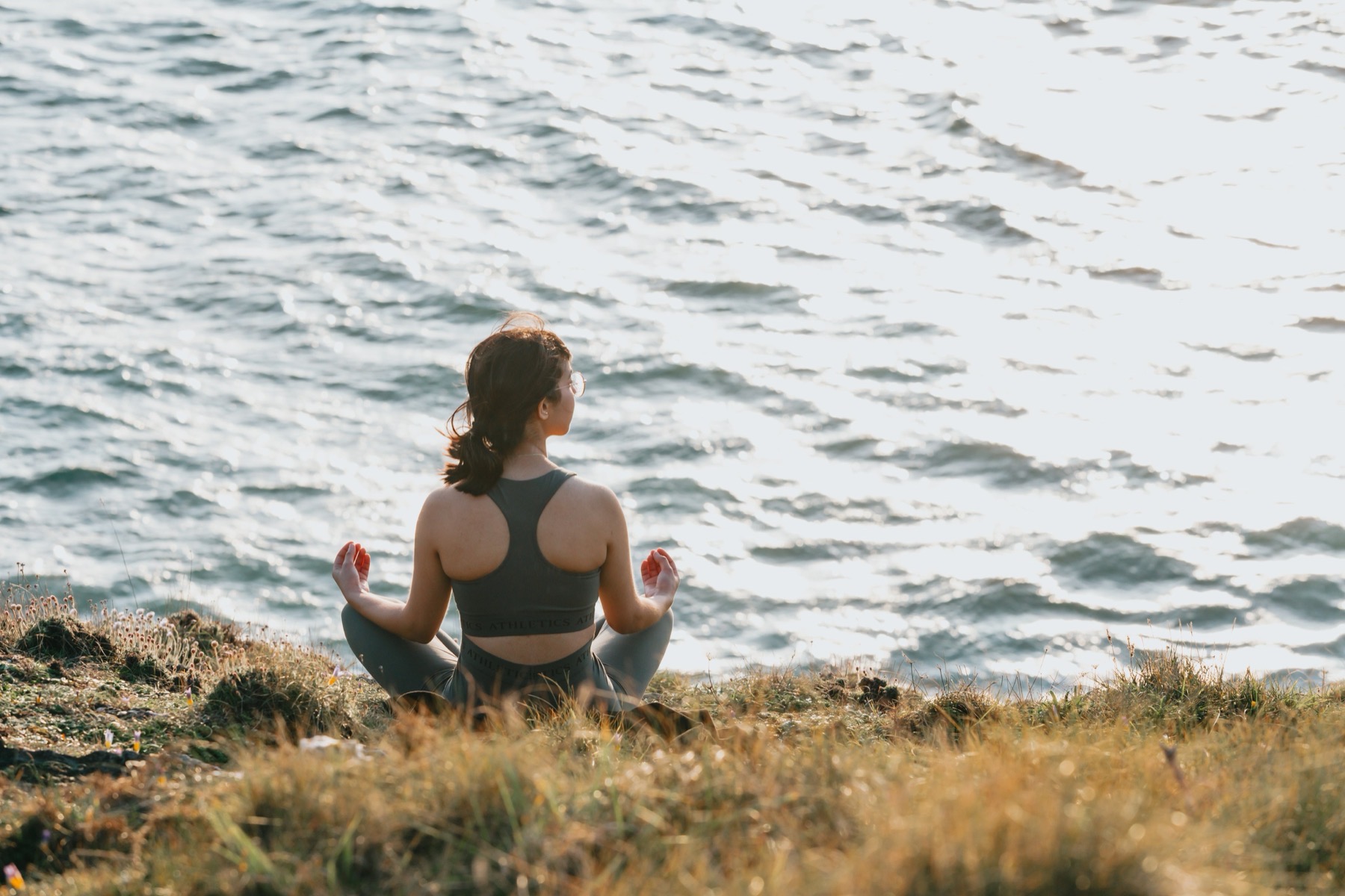 Woman sitting cross-legged facing the ocean